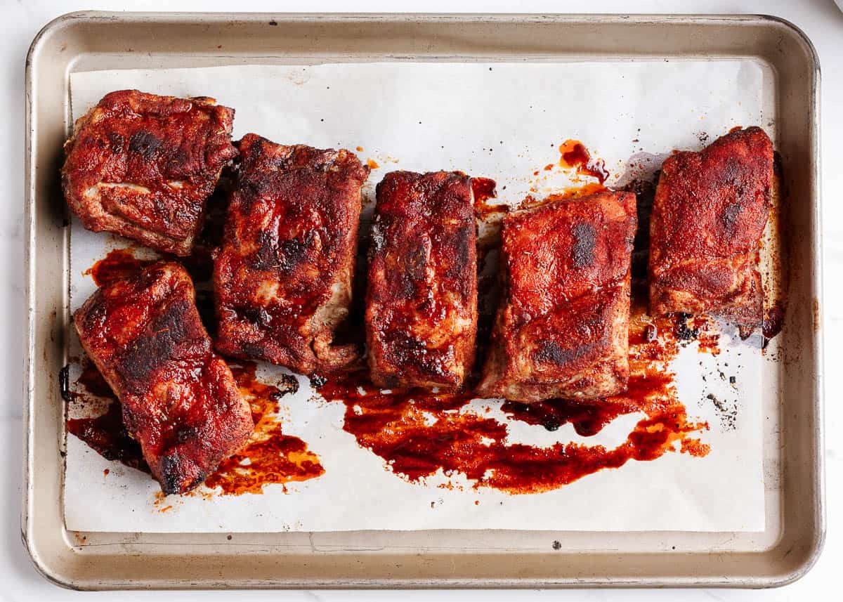 Slow Cooker Ribs - Easy baby back ribs smothered with a homemade rub and sweet and tangy barbecue sauce. Cooked to perfection in the crockpot and fall off the bone delicious. These are the best slow cooker ribs! ribs on baking sheet