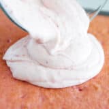 pouring strawberry cream frosting on top of cake