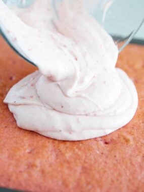 Pouring strawberry cream frosting on top of cake.