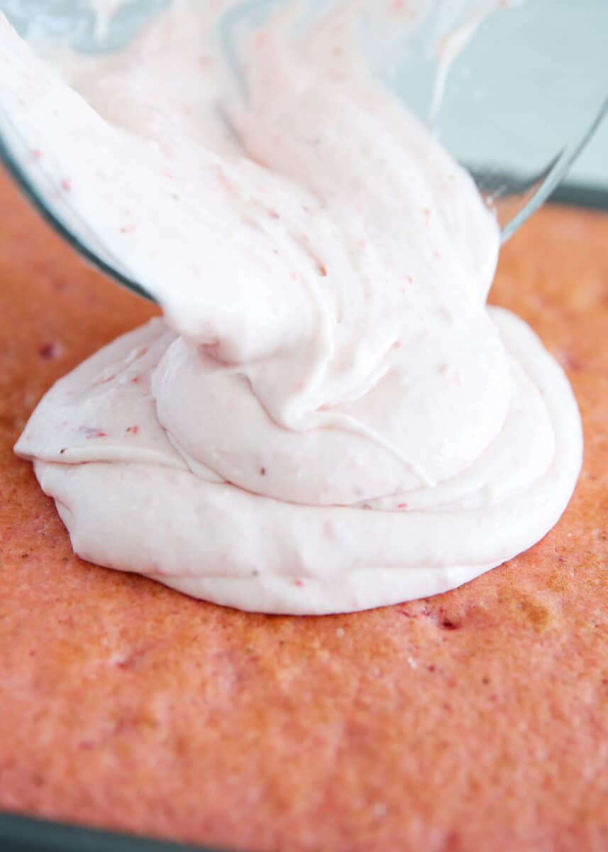 Pouring strawberry cream frosting on top of cake.