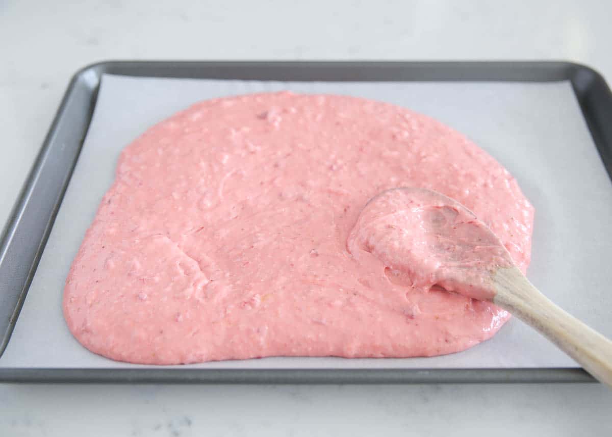Spreading strawberry cake batter infused with strawberry puree into a sheet cake pan.