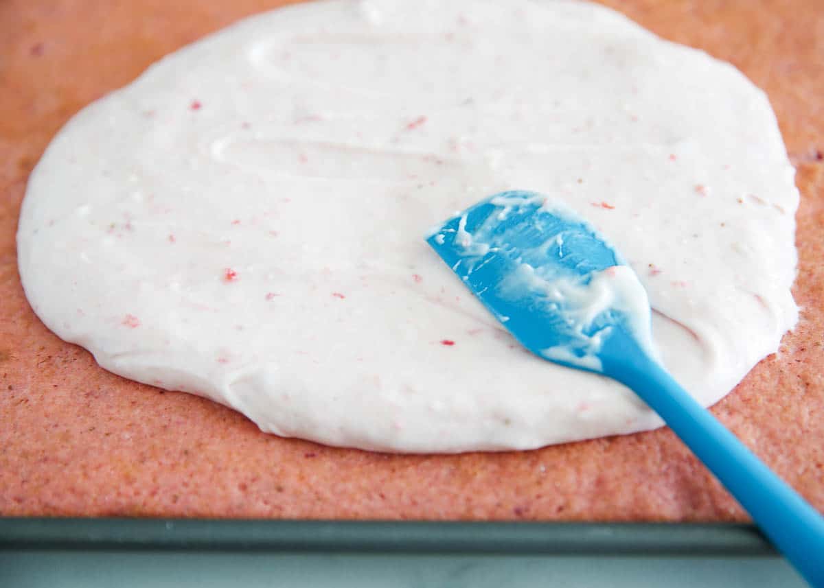 Spreading frosting on strawberry sheet cake.