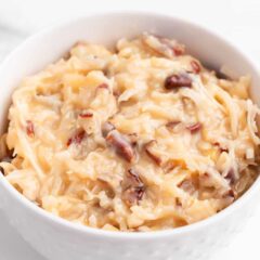 Coconut pecan frosting with shredded coconut and pecans in white bowl.