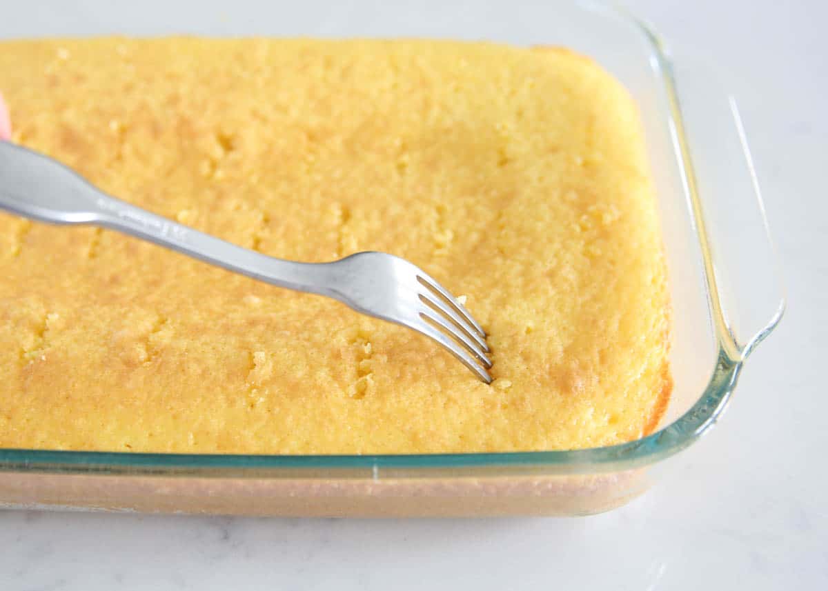 Poking a lemon poke cake with holes to prepare it for jello.