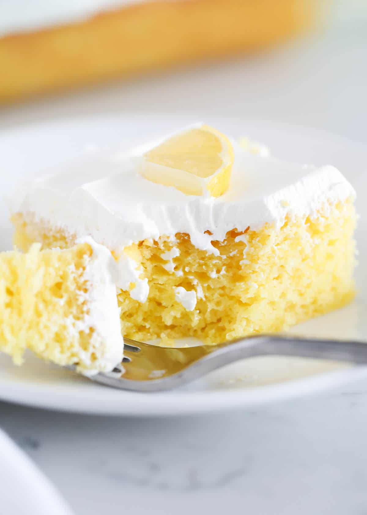 Slice of lemon cake with fork taking a bite. 