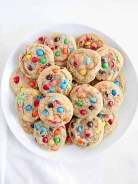 Stack of mini M&M cookies on a white plate.
