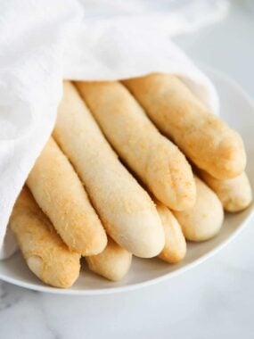 Olive Garden breadsticks recipe fresh from the oven wrapped in a white linen towel and placed on a serving plate.