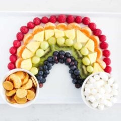 Rainbow fruit platter on white plate with a bowl of marshmallow and gold coins.