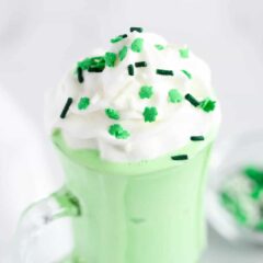 Homemade shamrock shake in a clear glass with whipped cream and sprinkles.