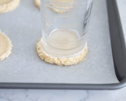 pressing sugar cookie down with a cup