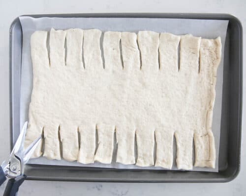 cutting strips in pizza dough on baking sheet