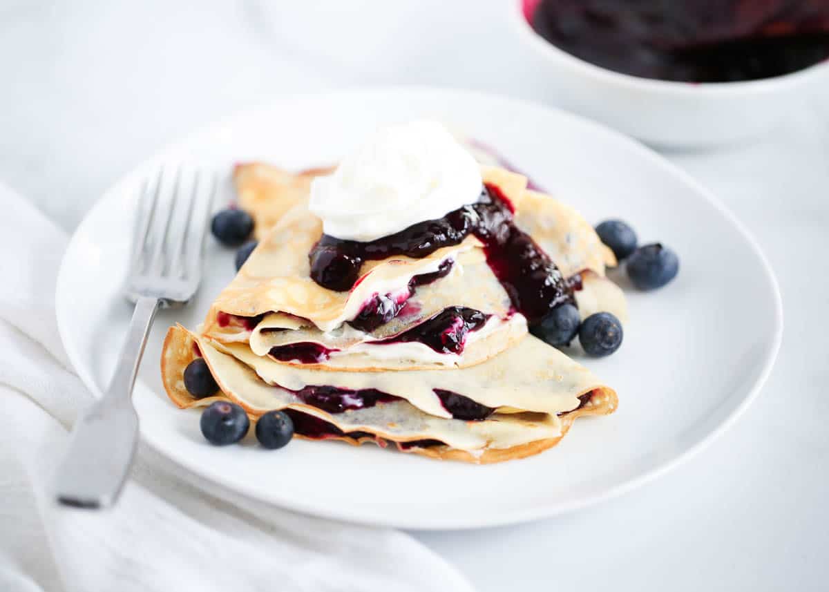 Stacked blueberry crepes on white plate.