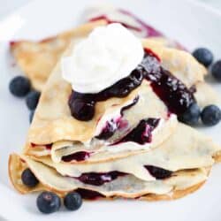 Stacked blueberry crepes on white plate.