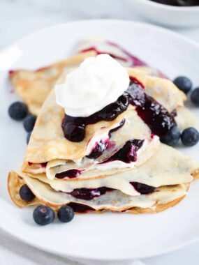Stacked blueberry crepes on white plate.