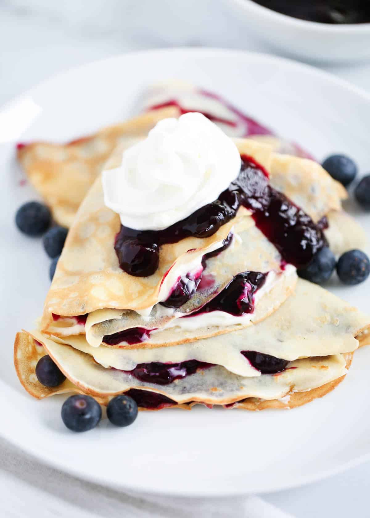 Stacked blueberry crepes on white plate.