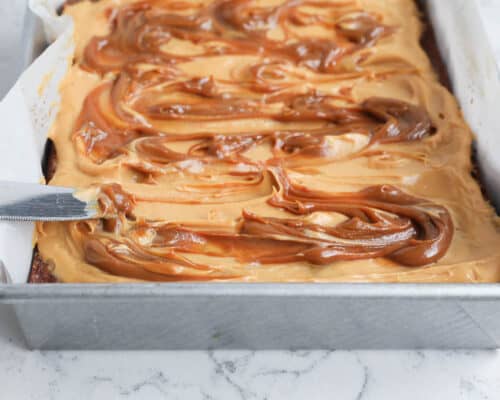 spreading caramel frosting on top of cake