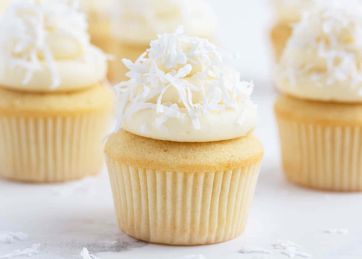 These coconut cupcakes are unbelievably moist and delicious! They are adorned with a crown of creamy coconut frosting sprinkled with sweetened coconut on top! coconut cupcakes on counter