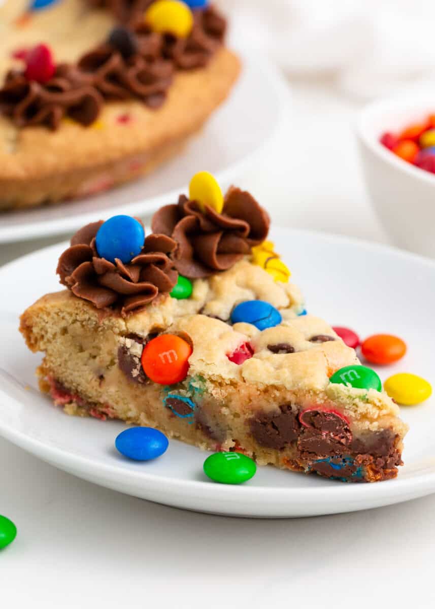 Slice of M&M cookie cake on white plate.