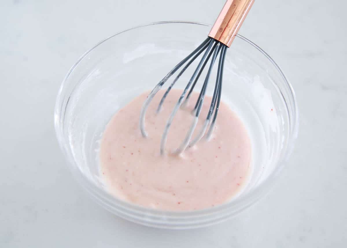 Whisking strawberry glaze in a glass bowl.