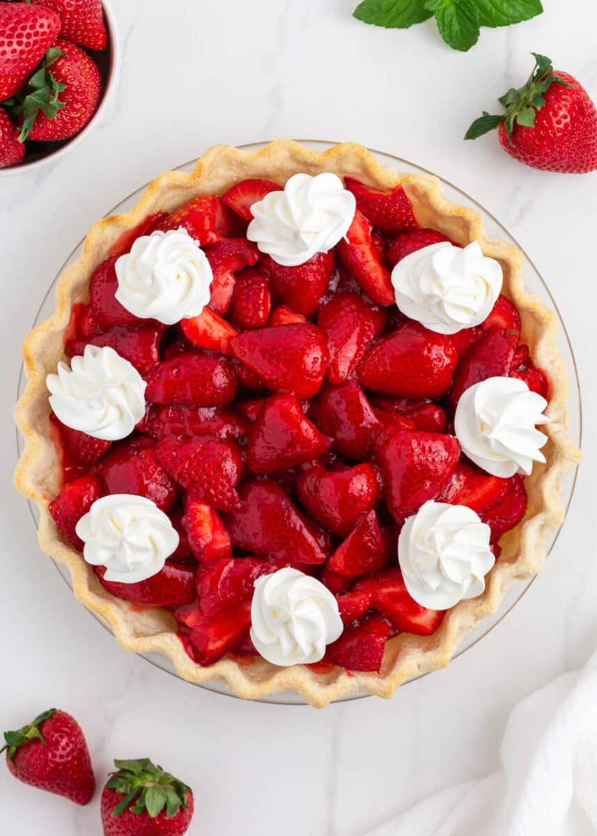 Fresh strawberry pie with whipped cream on a marble countertop.