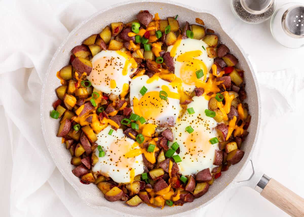 An easy 20-minute egg skillet made with crispy red potatoes, bacon, sautéed onions and peppers with over easy eggs on top. Perfect for breakfast, brunch or even dinner! Potatoes and eggs cooking in skillet.