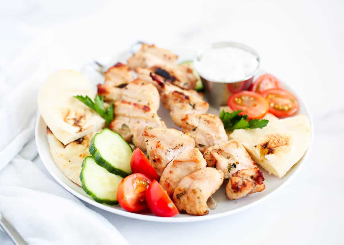 Chicken kabobs on plate with pita, tomatoes and cucumbers.