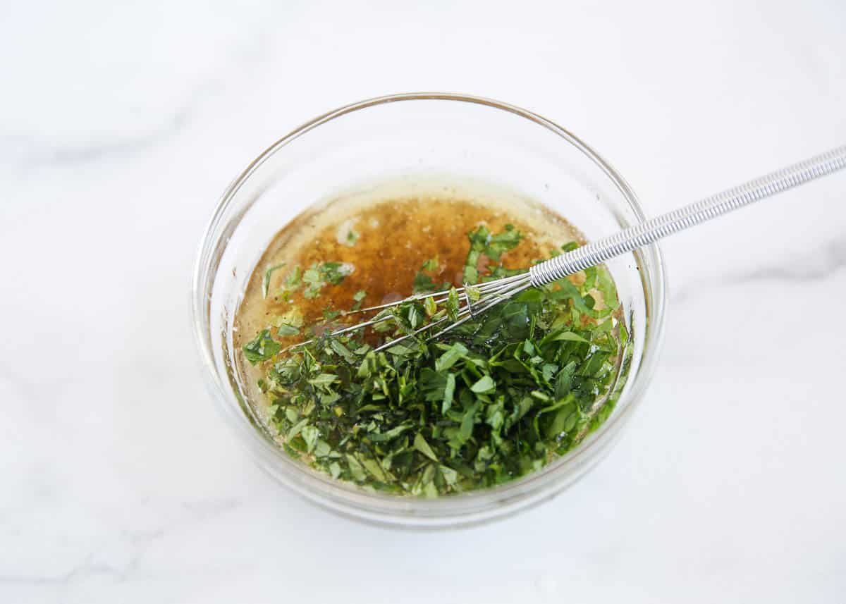Whisking olive oil and parsley in a glass bowl.
