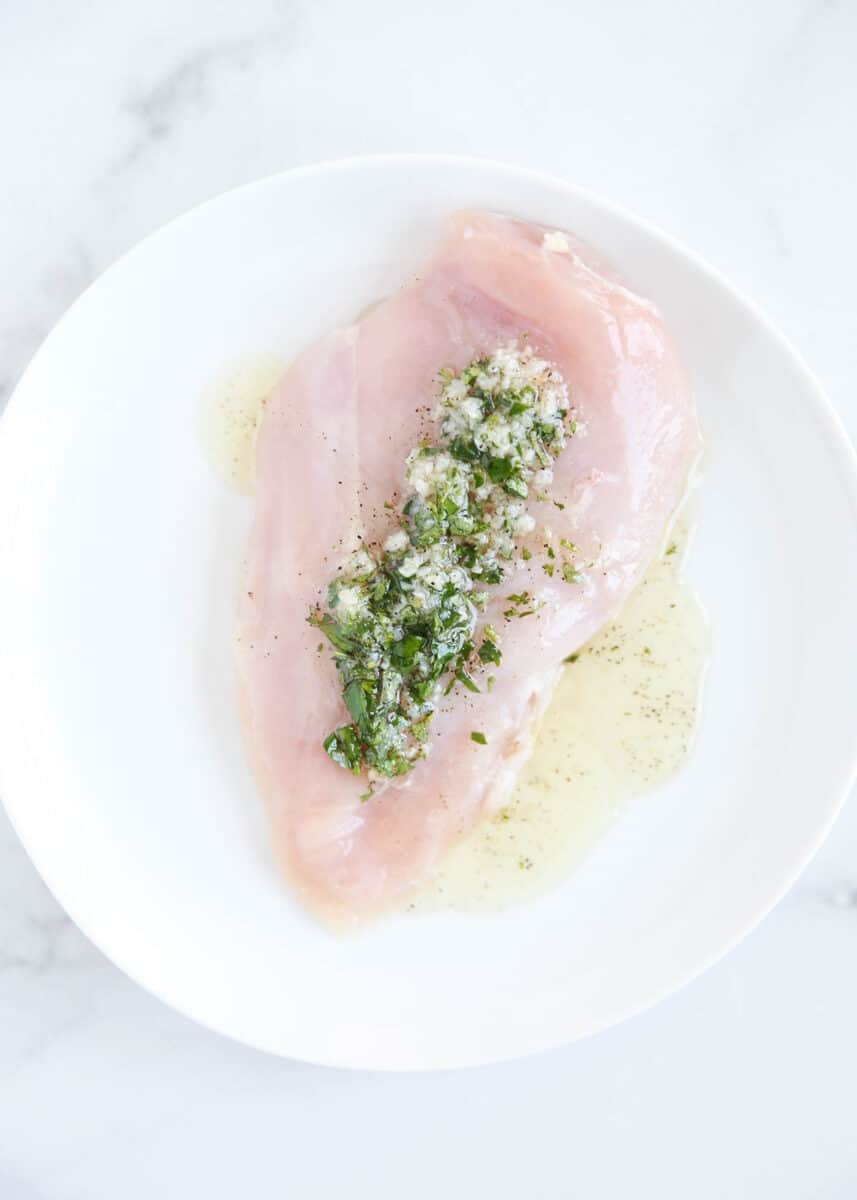 Chicken with Greek marinade on top on a white plate.