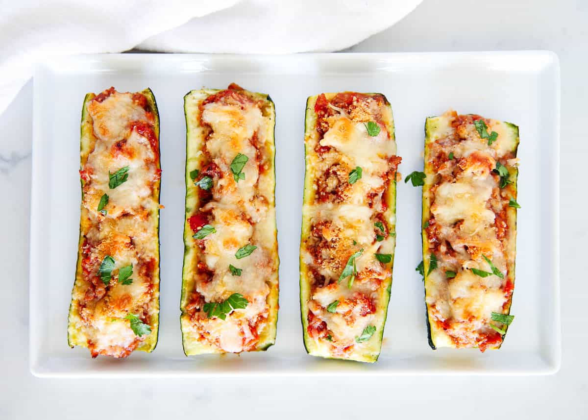 Stuffed zucchini boats on a white plate sitting on the countertop.