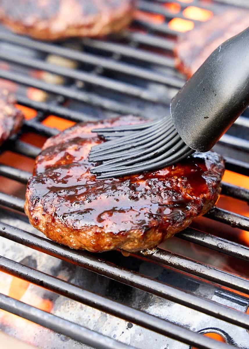 Brushing teriyaki sauce on hamburger cooking on the grill.