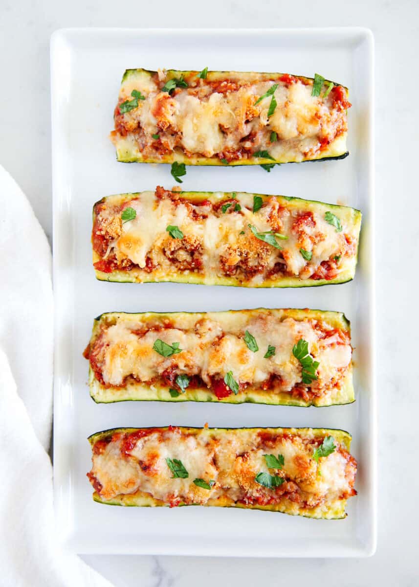 Zucchini boats with cheese on a white plate on the counter.