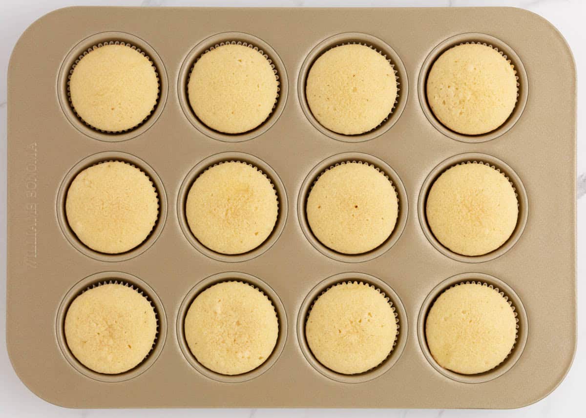 Baked coconut cupcakes cooling in a lined muffin pan.