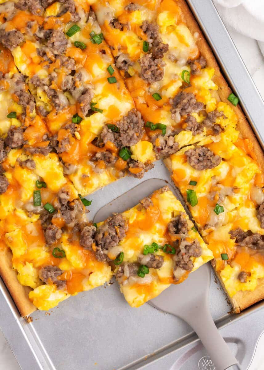 Breakfast pizza is a savory breakfast lover's dream! It's a complete breakfast on your table in under 30 minutes made with easy dough, eggs, sausage, and two kinds of melty cheese! Sliced sausage breakfast pizza on pan.