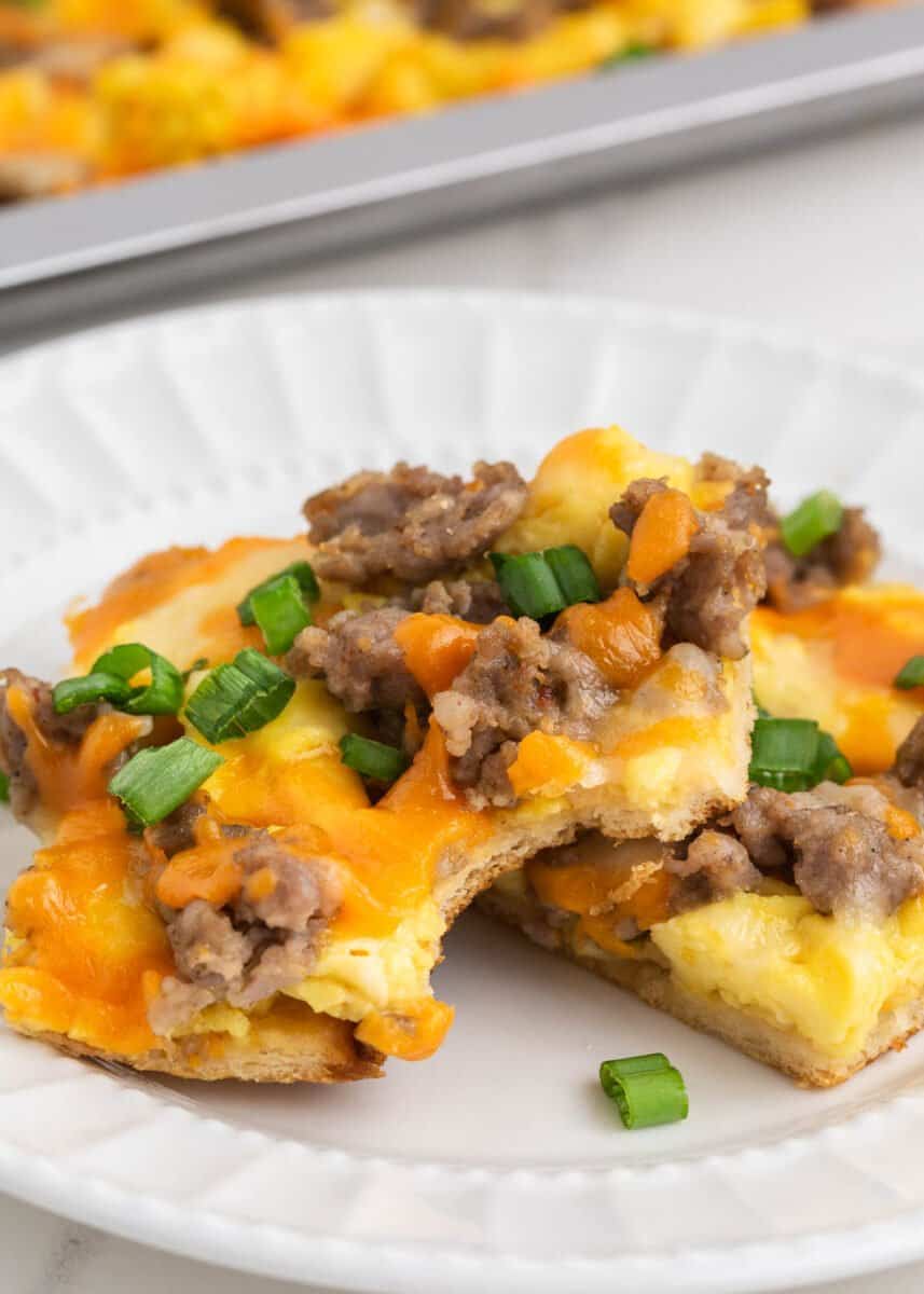 Breakfast pizza is a savory breakfast lover's dream! It's a complete breakfast on your table in under 30 minutes made with easy dough, eggs, sausage, and two kinds of melty cheese! Slice of sausage breakfast pizza on a white plate.