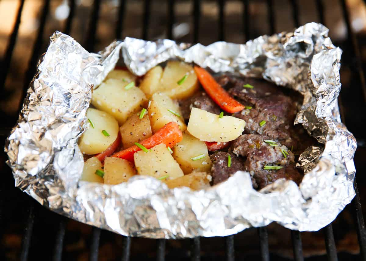Steak and potato foil packs cooking on grill.