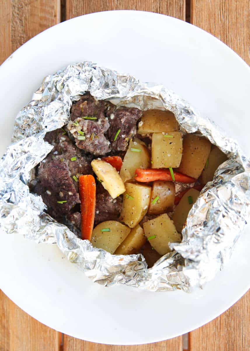 Steak and potato foil packs on wooden countertop.