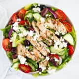 Greek chicken salad in a white bowl on marble counter.