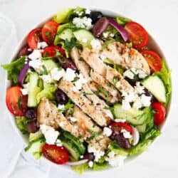 Greek chicken salad in a white bowl on marble counter.