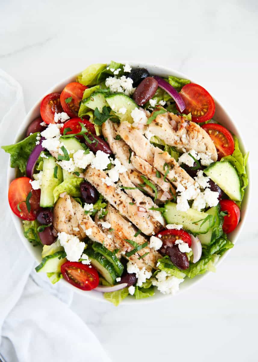 Greek chicken salad in a white bowl on marble counter.