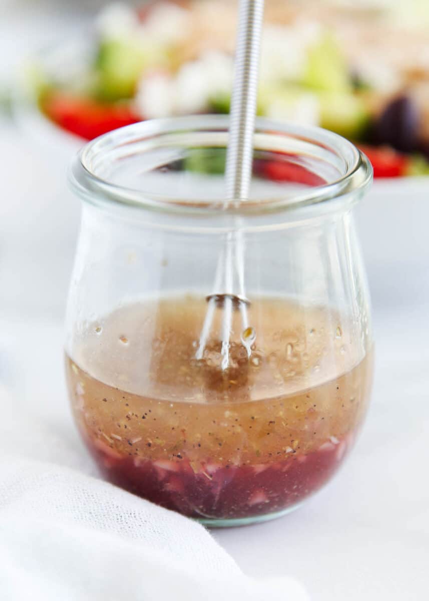 Whisking Greek salad dressing in a glass jar.