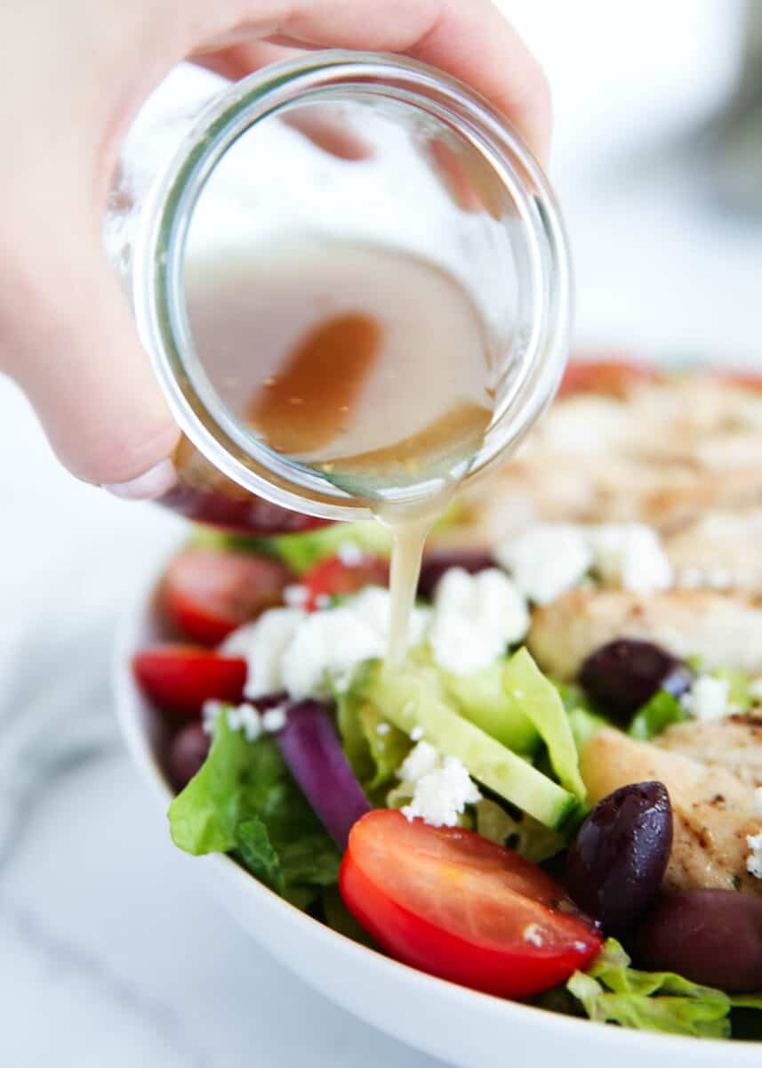 Pouring Greek salad dressing over a salad.