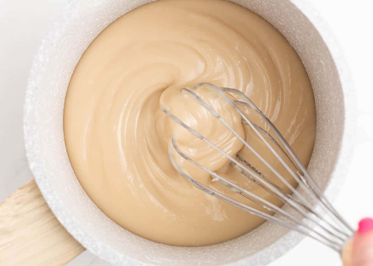 This smooth maple glaze is infused with sweet maple syrup and is the perfect way to make your desserts next level delicious. Use on donuts, cookies, cake, cinnamon rolls and more! Whisking maple glaze in a pot.