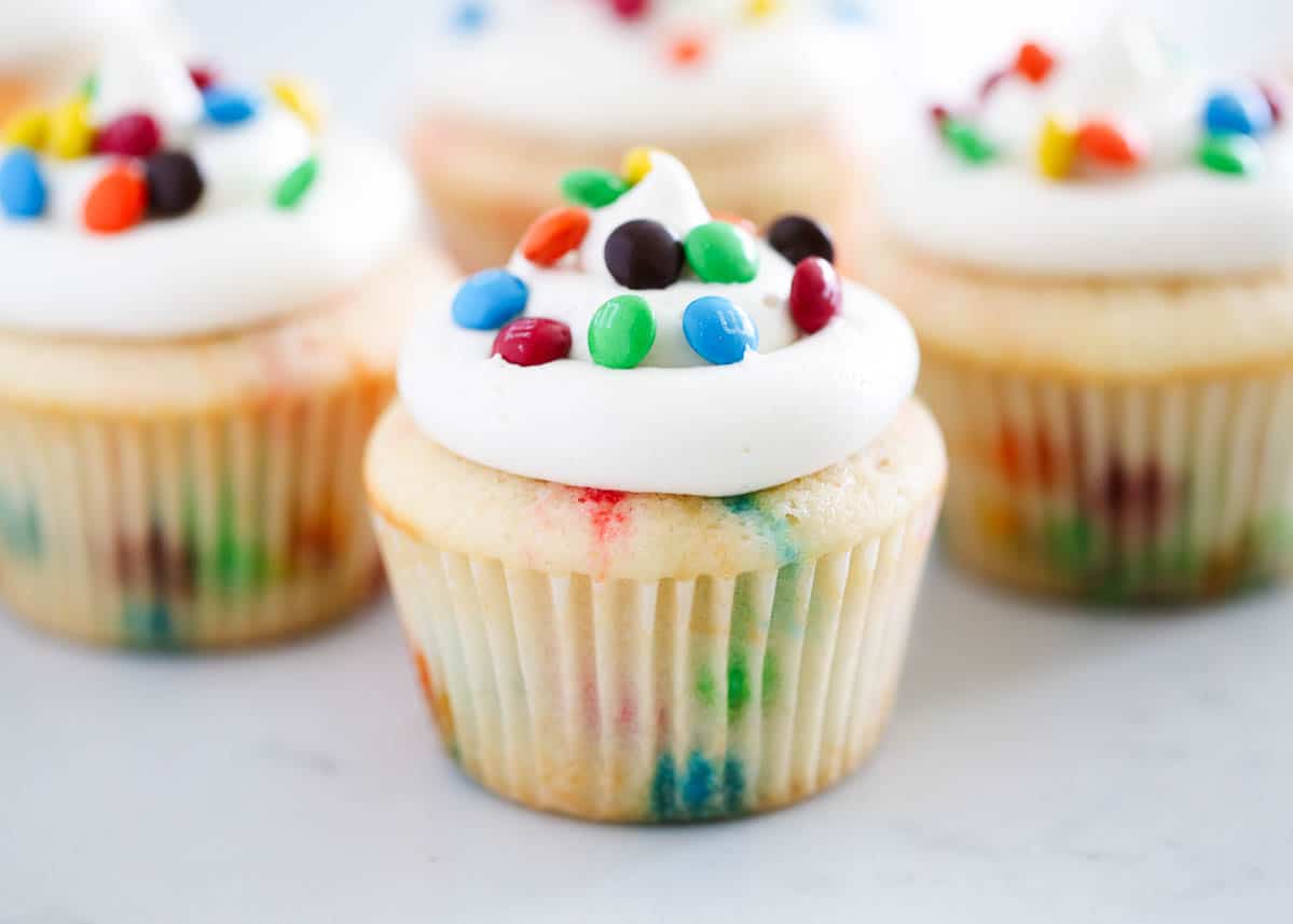 These bright and colorful M&M cupcakes are super soft and moist thanks to the cake flour, sour cream, and buttermilk. Topped with a homemade vanilla frosting or classic buttercream, these fun and festive cupcakes can be ready in just 30 minutes! M&M cupcakes on marble counter.