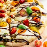 Sliced caprese pizza drizzled with balsamic glaze on pizza peel.