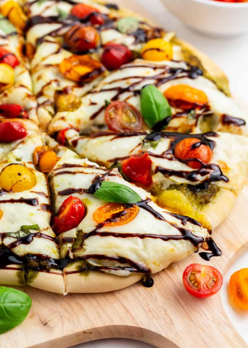 Sliced caprese pizza drizzled with balsamic glaze on pizza peel.