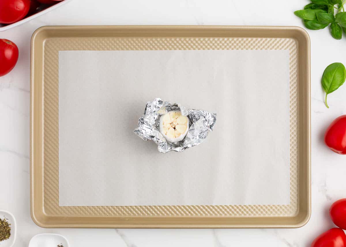Garlic cloves wrapped in foil on baking sheet.
