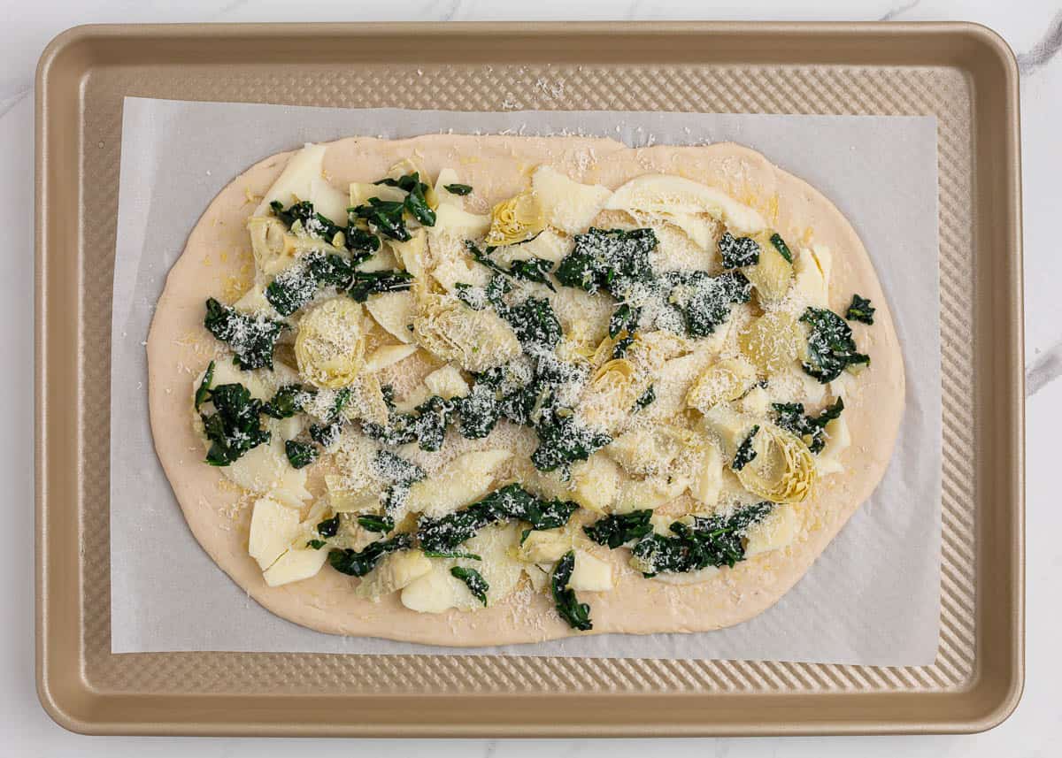 Cooking spinach artichoke pizza on baking sheet.