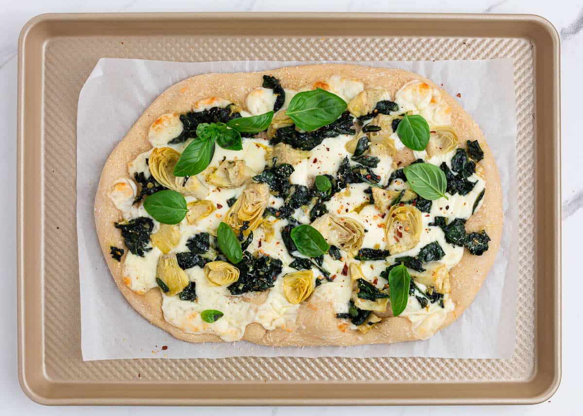 Spinach artichoke pizza on baking sheet.