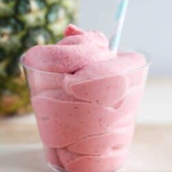 Strawberry dole whip in a clear cup on wooden surface.