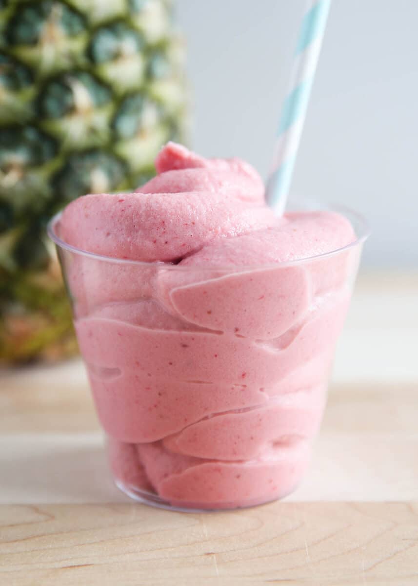 Strawberry Dole Whip in a clear cup on wooden surface.